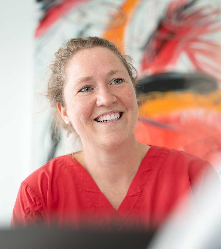 Lächelnde Dr. Juliane Simon in rotem Schlupfkasack vor großem Gemälde