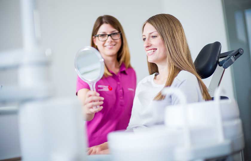 Mitarbeiterin hält kleinen Spiegel für lächelnde Patientin