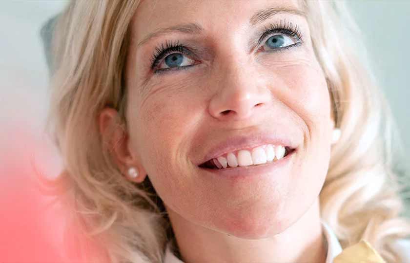 Geischt einer lächelnden blonden Dame, die auf dem Behandlungsstuhl sitzt.