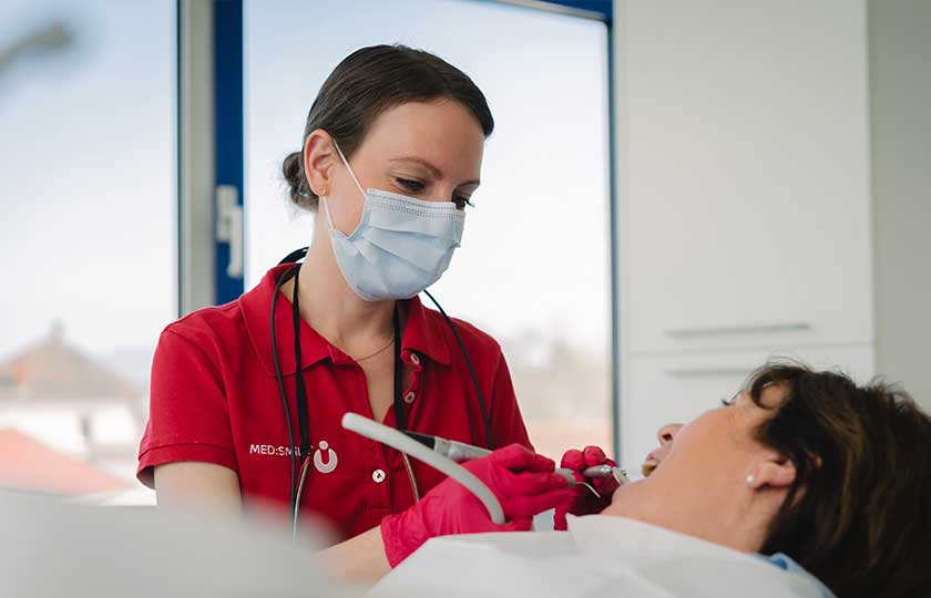 MFA bei der Entfernung von Belägen mit zahnmedizinischen Geräten bei einer Patientin auf Behandlungsstuhl im Rahmen einer Parodontitis-Behandlung.