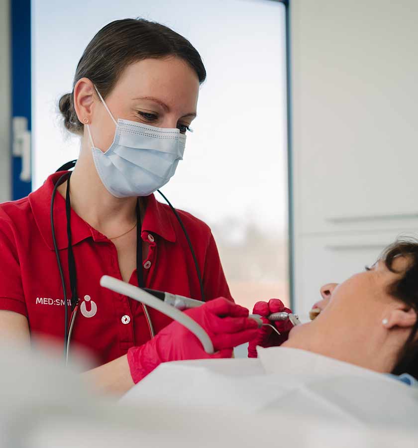 Behandlerin mit Mundschutz und Reinigungsgerät in der Hand bei der Parodontitis-Behandlung einer Patientin auf Behandlungsstuhl.