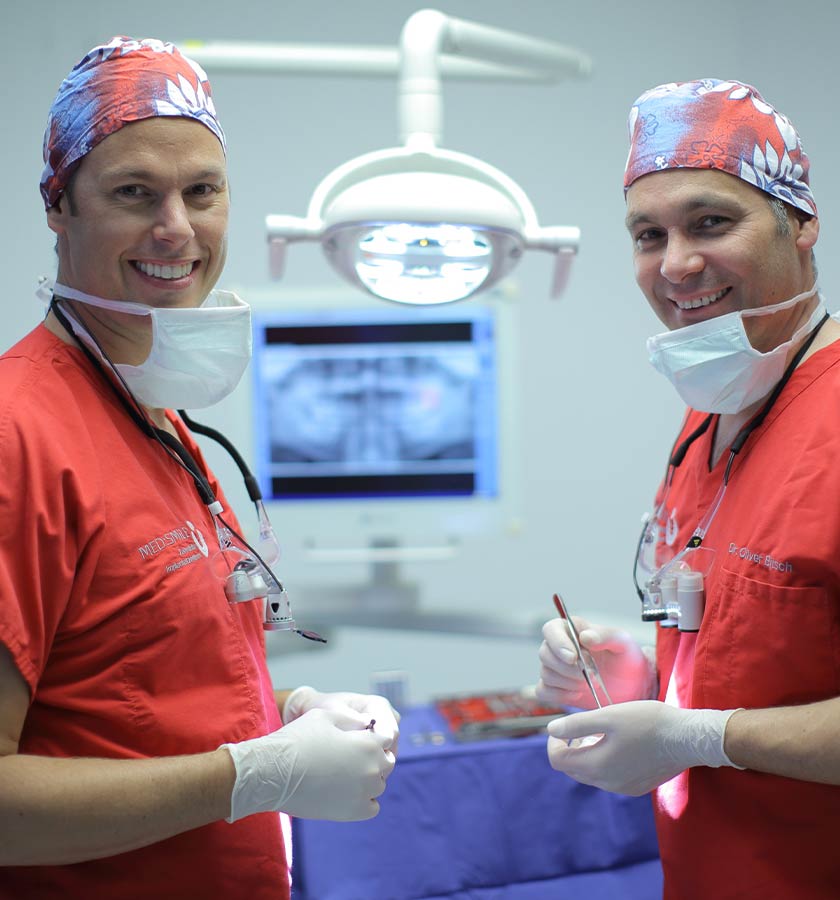 Dr. Jäger und Dr. Bitsch im OP mit OP-Lampe und Röntgenbild im Hintergrund.