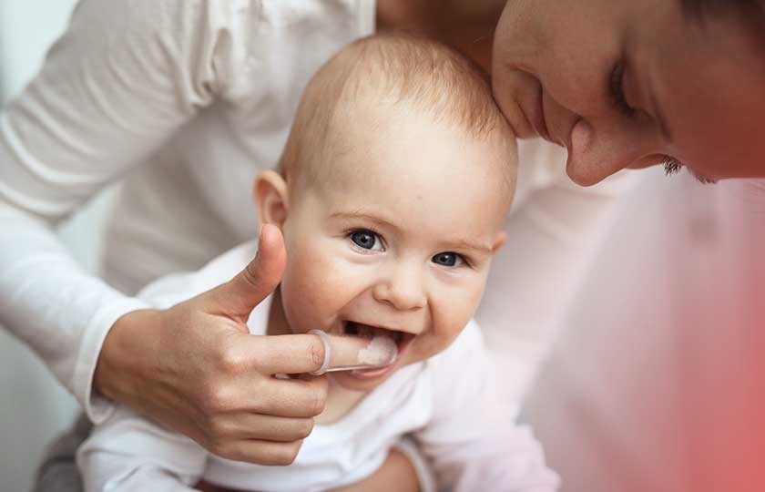 Lächelndes Baby im Arm der Mutter, die nach den Zähnen des Babys schaut