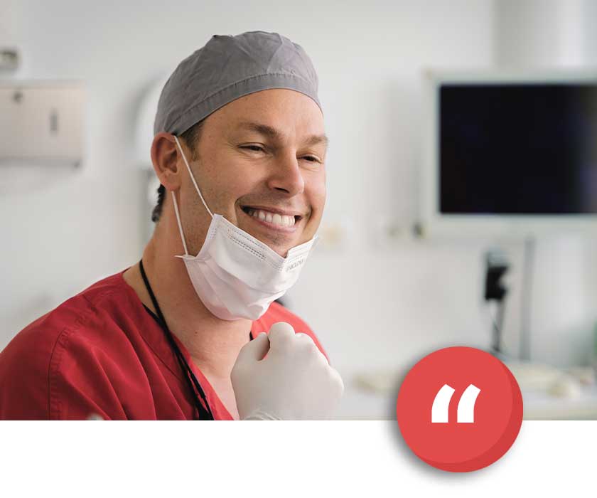 Dr. Daniel Jäger von MED:SMILE mit grauer OP-Mütze und Mundschutz vor Monitor im Behandlungsraum
