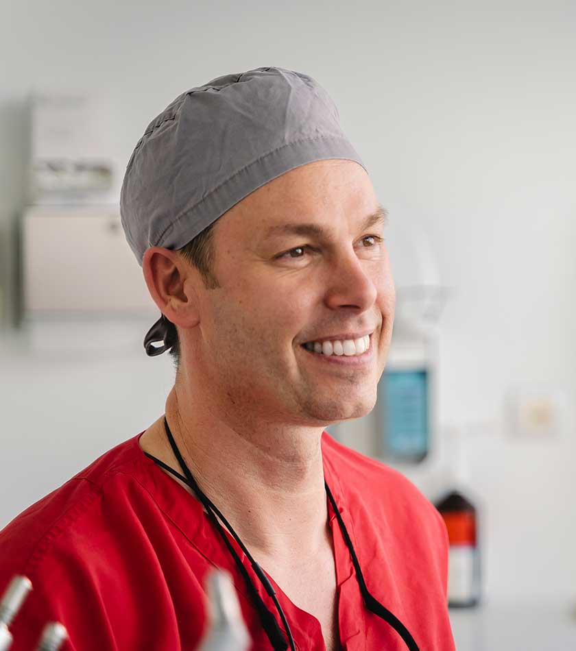 Dr. Daniel Jäger mit grauer OP-Haube im Behandlungszimmer. 