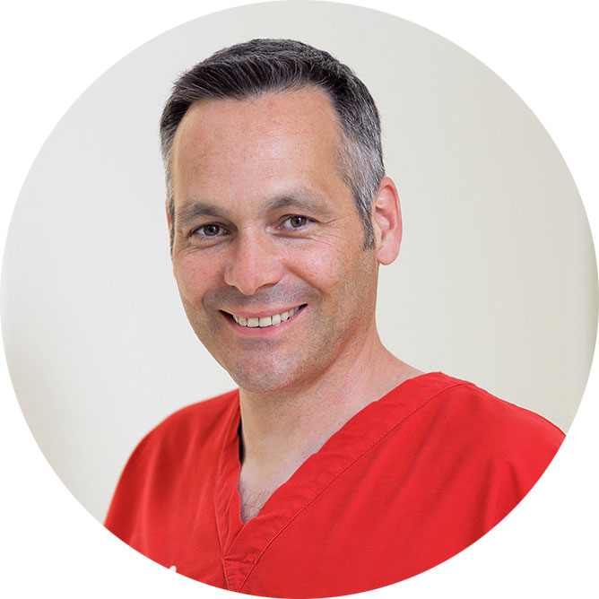 Rundes Portraitbild von Zahnarzt Dr. Oliver Bitsch mit rotem Schlupfkasack