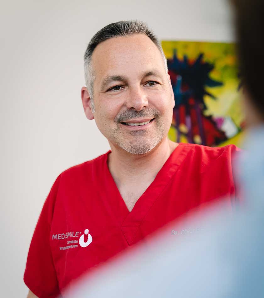 Dr. Oliver Bitsch in rotem Schlupfkasack mit MED:SMILE-Logo im Gespräch