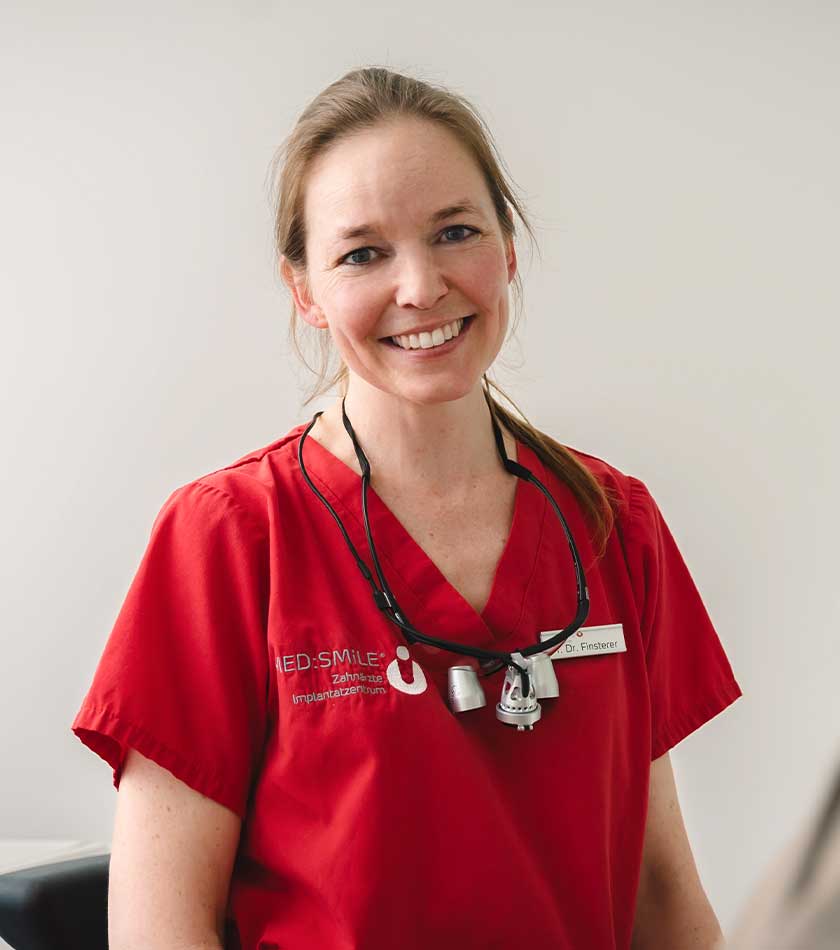 Dr. Romy Finsterer in rotem Schlupfkasack und Lupenbrille um den Hals.