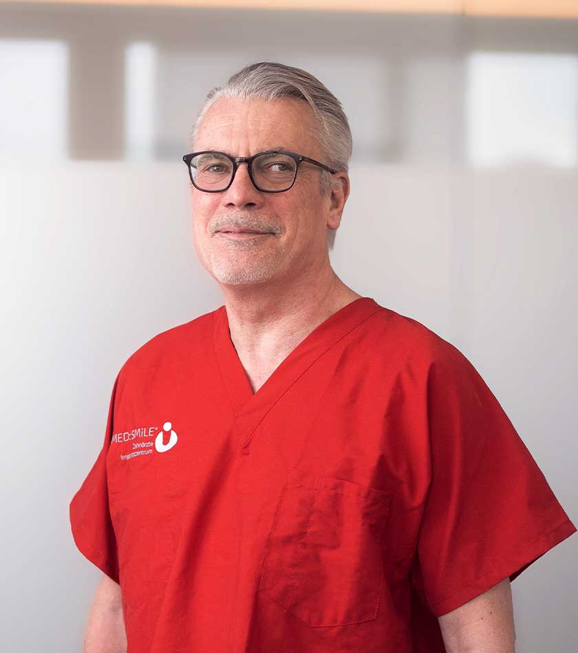 Zahnarzt Peter Krüger von MED:SMILE in rotem Schlupfkasack